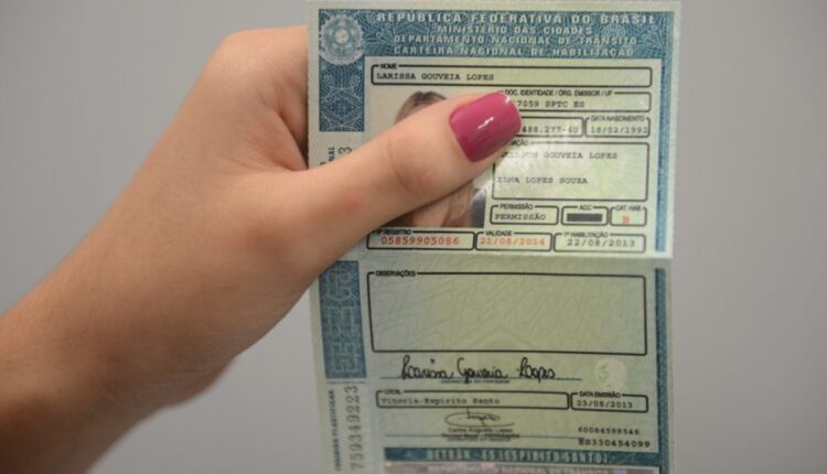 Mulher com as unhas pintadas segurando a Carteira Nacional de Habilitação