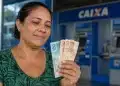 Mulher observa cédulas de real em frente a uma agência da Caixa, representando os pagamentos do Bolsa Família entre os dias 22 e 24 de julho.