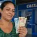 Mulher observa cédulas de real em frente a uma agência da Caixa, representando os pagamentos do Bolsa Família entre os dias 22 e 24 de julho.