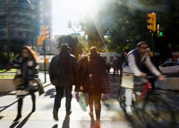 Pedestres e ciclista atravessando a faixa de pedestres em dia ensolarado com semáforo verde para pedestres.