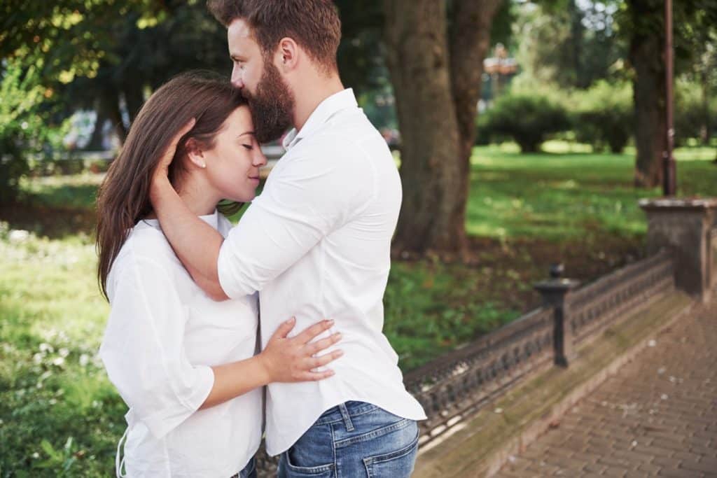 Um homem abraçado a uma mulher beijando sua testa ao ar livre