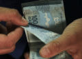 Mãos contando cédulas de cem reais recebidas pelo Saque Calamidade do FGTS