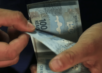 Mãos contando cédulas de cem reais recebidas pelo Saque Calamidade do FGTS