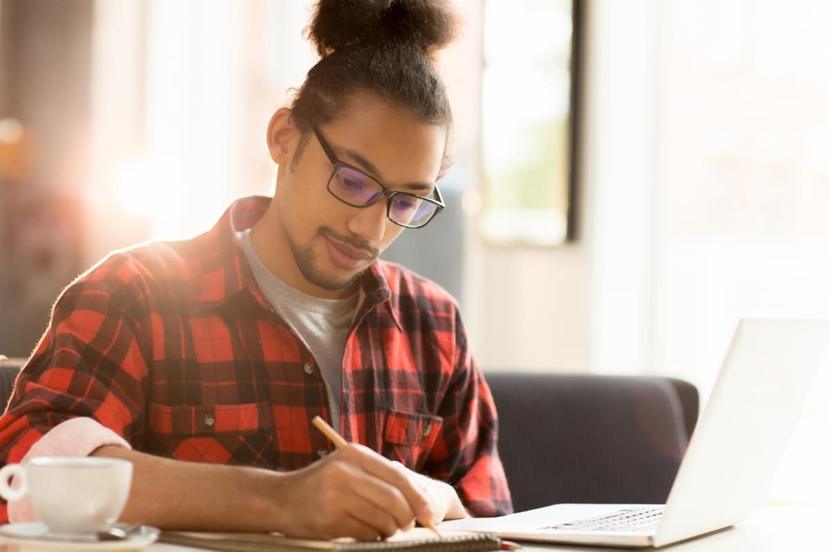 Pessoa estudando com um notebook e anotando em caderno, simbolizando o aprendizado das novas regras ortográficas.