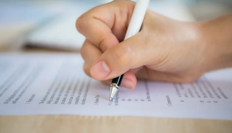 Mão preenchendo uma ficha de inscrição para um processo seletivo