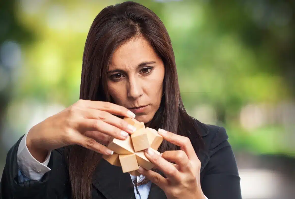 Mulher concentrada montando um quebra-cabeça de madeira, representando lógica e determinação.