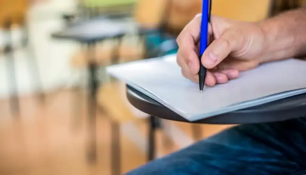 Mão segurando uma caneta, pronta para escrever em uma folha de papel em um ambiente de estudo
