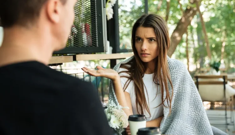 Mulher com expressão de desconfiança durante uma conversa, levantando a mão em um gesto questionador, enquanto um homem fala.
