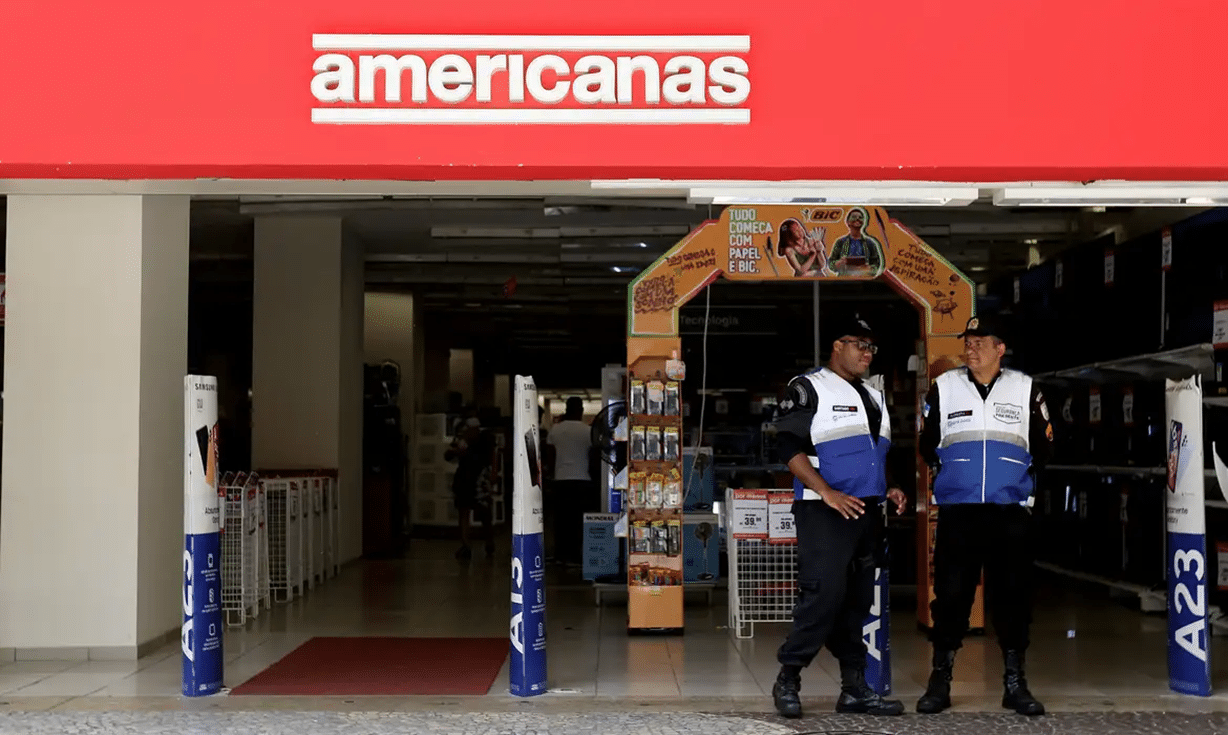 Entrada da loja das Americanas, com segurança na porta e ambiente visível no interior da loja.