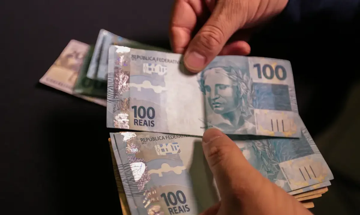 Notas de dinheiro de R$ 100 e R$ 200 empilhadas, simbolizando o saque do FGTS.