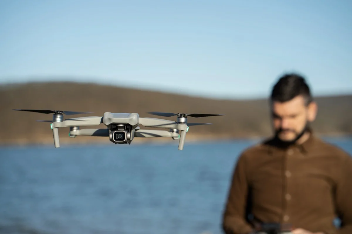 Drone voando sobre uma paisagem com um profissional no fundo, representando a profissão de engenheiro de drones.