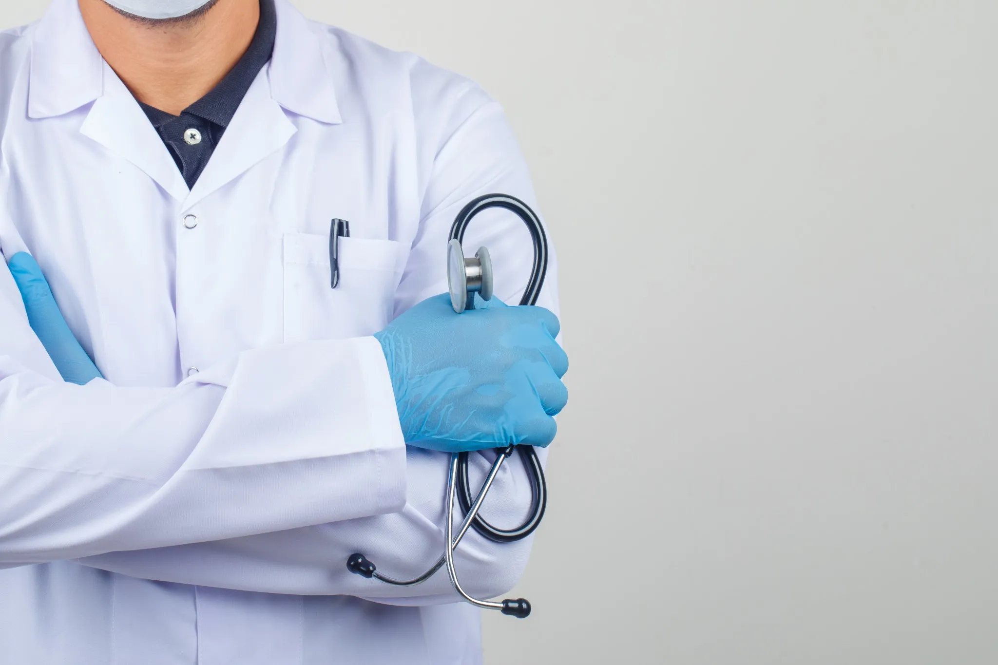 Médico de jaleco segurando um estetoscópio com luvas azuis.