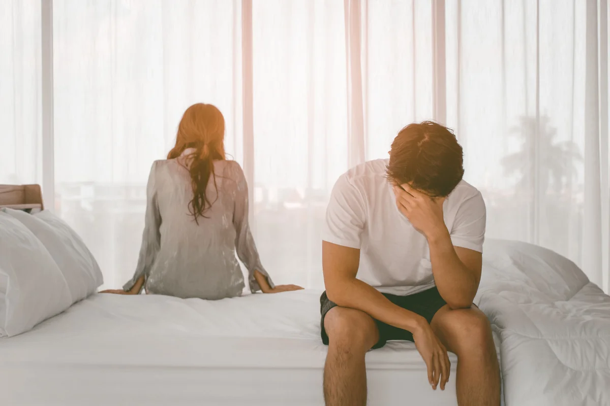 Casal afastado na cama, com um clima de tristeza e distanciamento, representando conflitos emocionais em um relacionamento.