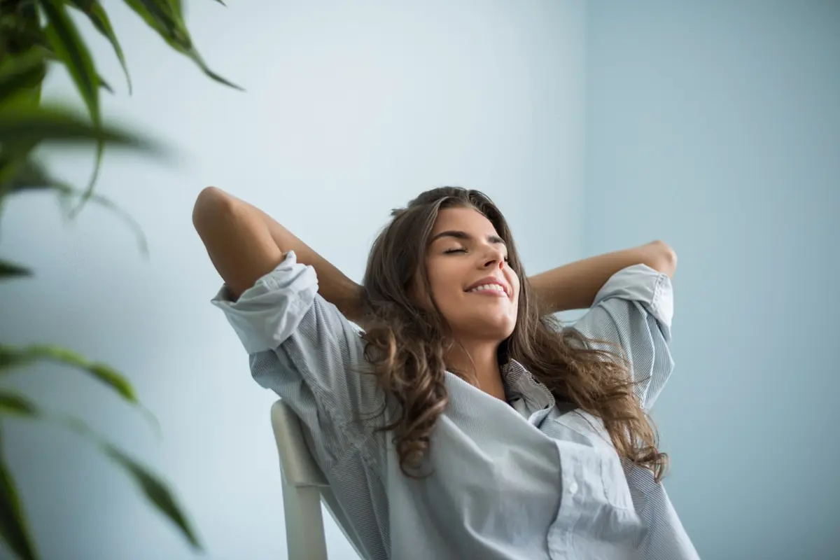 Mulher relaxada com expressão tranquila, de braços cruzados atrás da cabeça.
