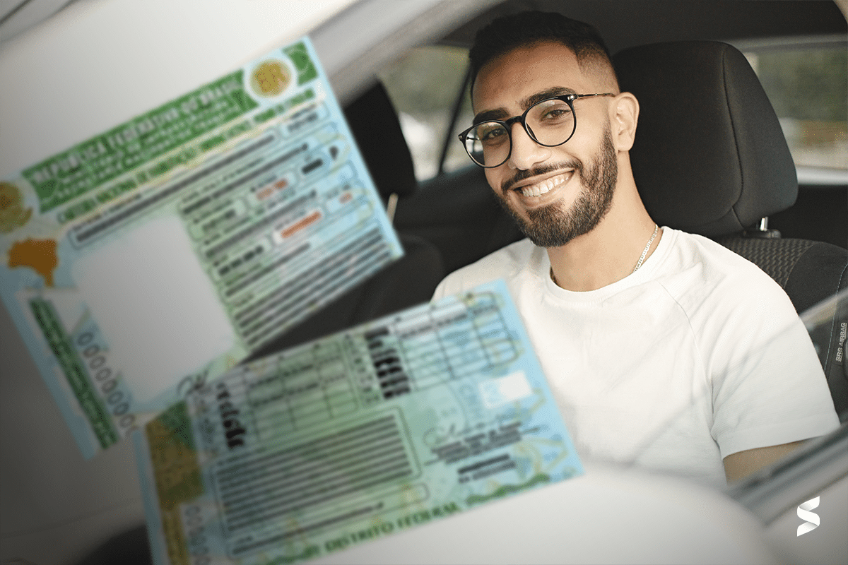 Jovem sorrindo dentro de um carro, segurando sua carteira de habilitação, representando o atendimento do Detran para a CNH popular.