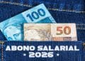 Cédulas de R$ 100 e R$ 50 saindo do bolso de uma calça jeans, representando o pagamento do Abono Salarial 2026
