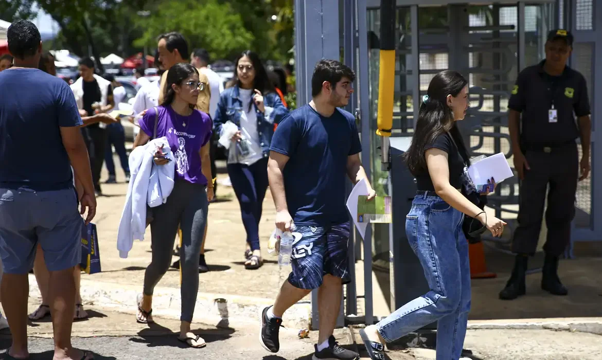 Grupo de pessoas chegando para realizar atividades em evento, com foco em jovens se dirigindo à entrada do local.