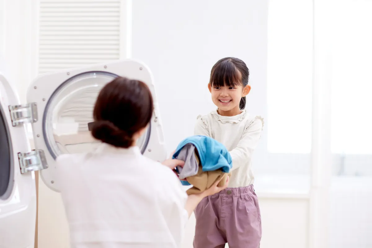 Criança sorridente ajudando a mãe com a roupa na lavanderia.