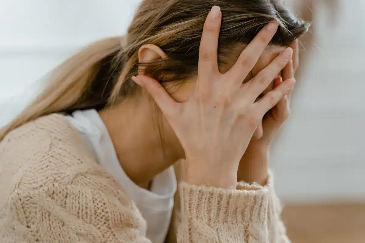 Mulher com as mãos na cabeça, visivelmente angustiada, em um ambiente interno.