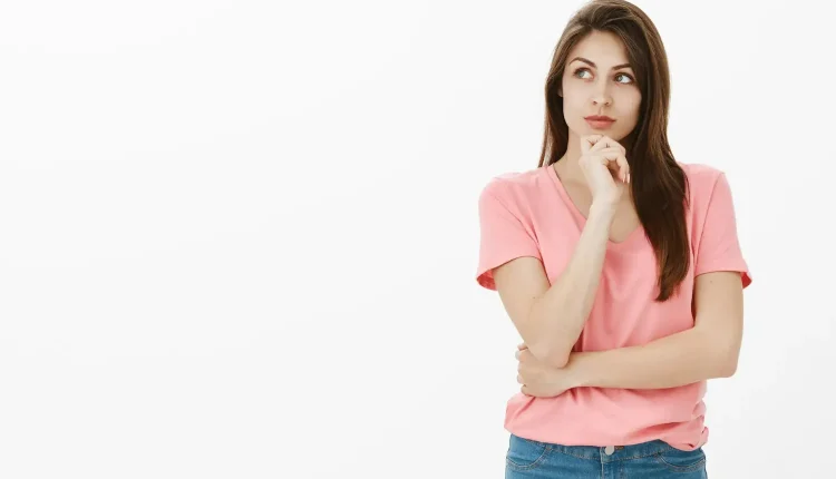 Mulher pensativa com camiseta rosa, olhando para o lado, sobre fundo branco.