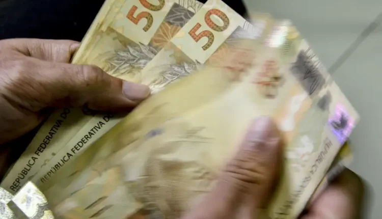 Pessoa segurando cédulas de 50 reais, simbolizando o saque de até R$ 2.900 disponível para brasileiros
