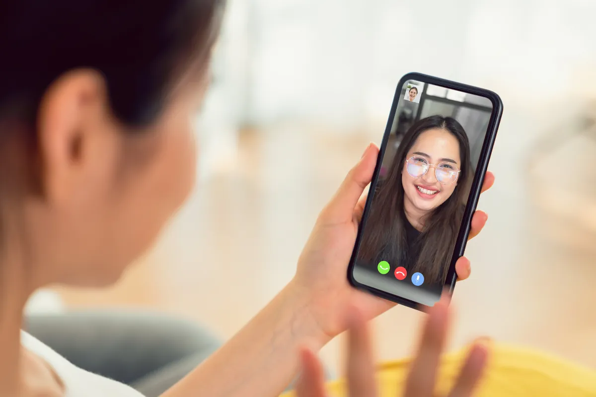 Mulher em chamada de vídeo pelo celular com amiga sorridente na tela.