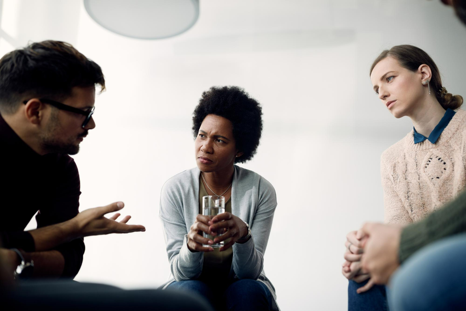 Grupo de pessoas em conversa séria, demonstrando atenção e linguagem corporal reflexiva durante discussão.