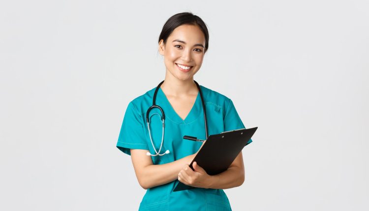 Enfermeira sorrindo e segurando um prontuário, com uniforme de saúde e estetoscópio no pescoço.