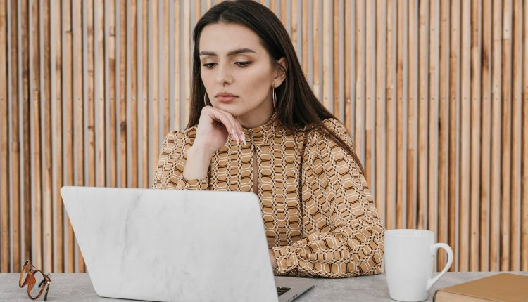 Mulher concentrada trabalhando em notebook em ambiente moderno com parede de madeira.