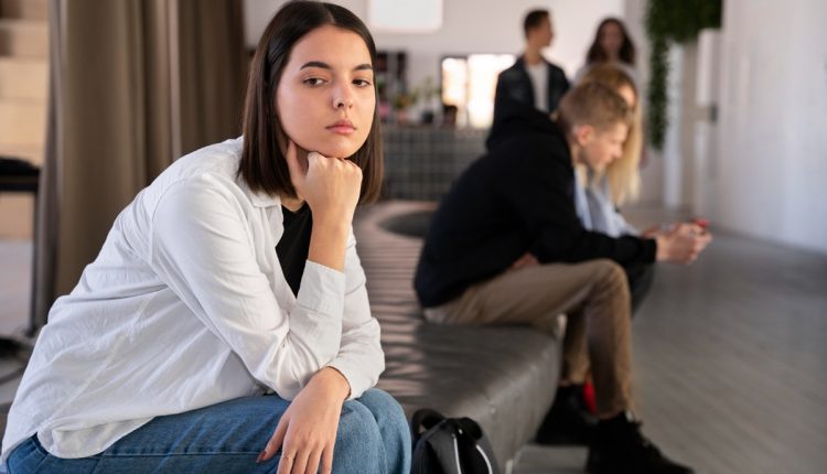 Mulher pensativa observando ao longe em um ambiente com outras pessoas ao fundo