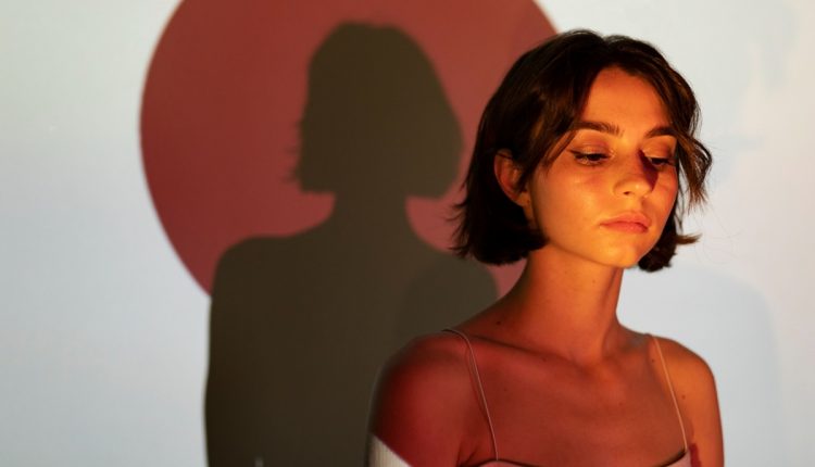 Jovem mulher com sombra projetada em parede, expressando introspecção.