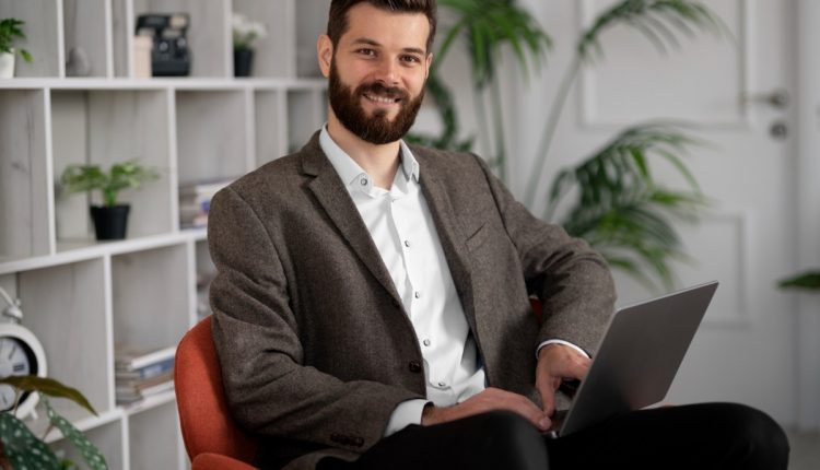 Homem sorridente em terno sentado em uma cadeira com laptop, representando cargos de alto nível no Brasil.