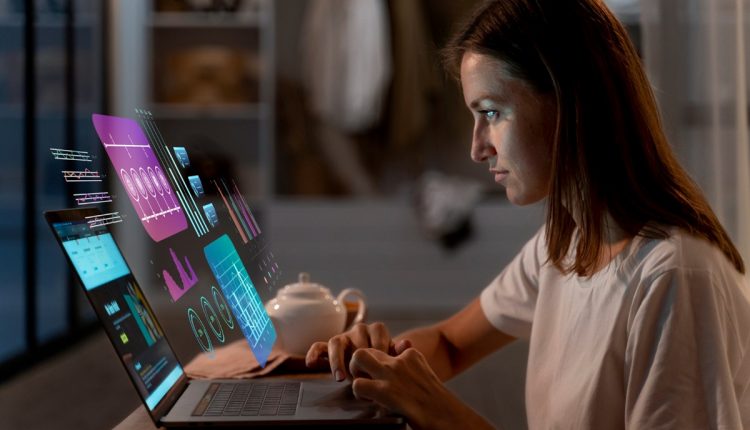 Mulher utilizando laptop com gráficos e dados digitais holográficos projetados.