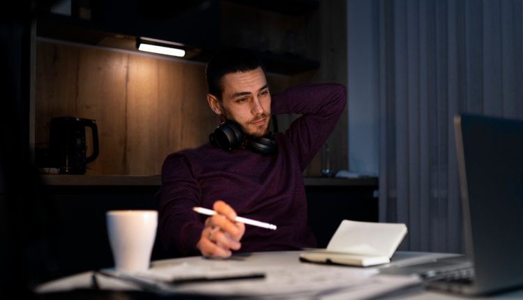 Homem pensativo trabalhando à noite em escritório com notebook e caderno.
