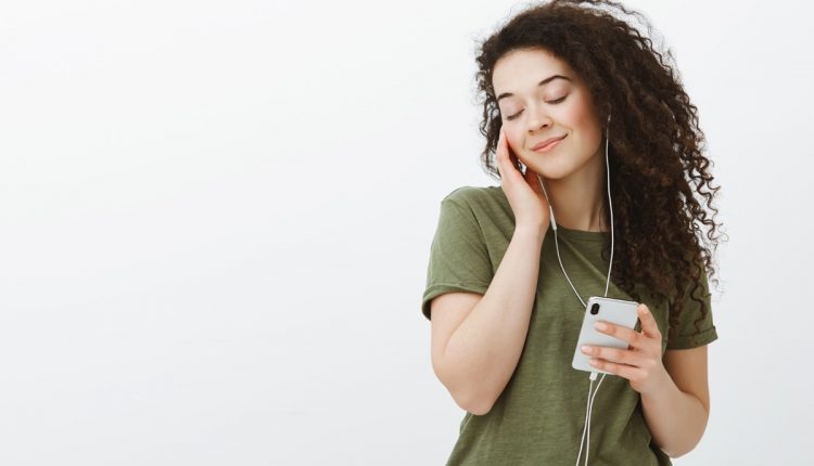 Mulher ouvindo música no celular com expressão serena, conectando emoções e sentimentos.