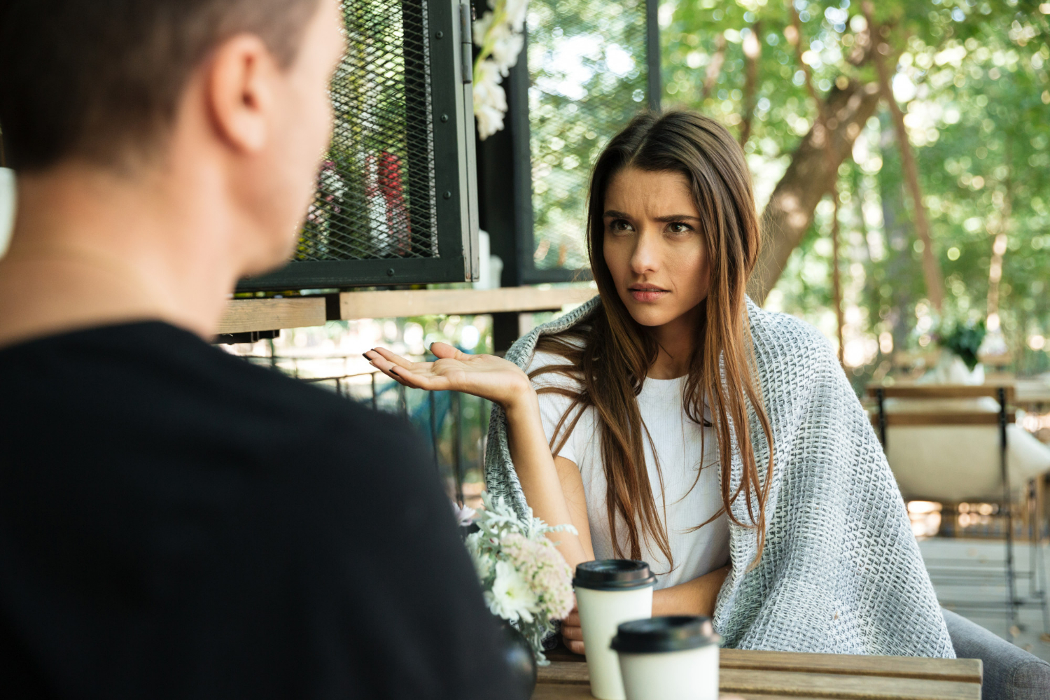 Mulher expressando frustração e questionamento durante uma conversa séria em um café.