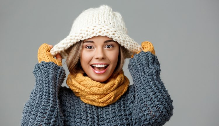 Mulher feliz usando roupas de inverno, incluindo suéter, cachecol e chapéu de tricô, representando a preferência pelo frio.