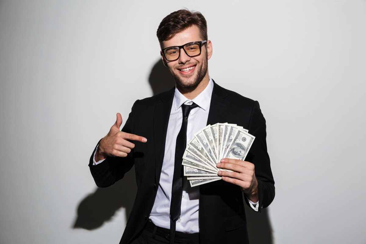 Homem em terno segurando uma pilha de notas de dólar e sorrindo, representando o crescimento do cargo de Diretor de Receita.