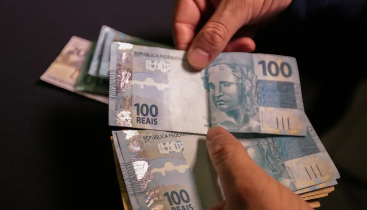 Mãos contando cédulas de R$ 100, dinheiro em espécie em destaque