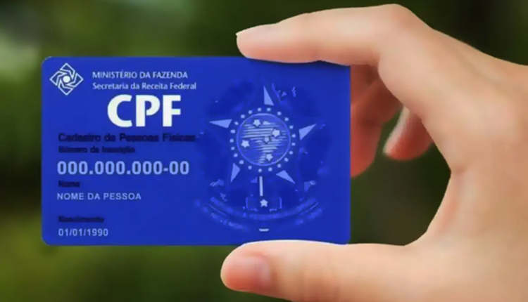 Pessoa segurando cartão azul do CPF com informações pessoais para comprovação de inscrição.