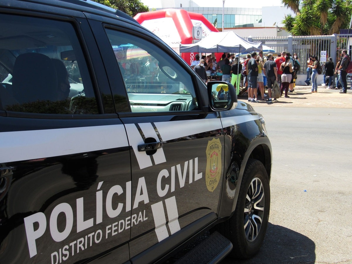 Viatura oficial da Polícia Civil do Distrito Federal estacionada em frente a evento com várias pessoas.