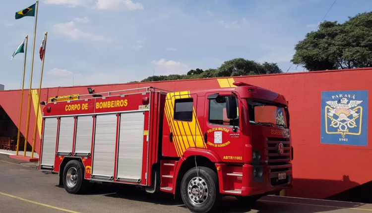 Caminhão do Corpo de Bombeiros do Paraná estacionado em frente a prédio vermelho com bandeiras