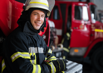 Bombeiro sorridente pronto para ação ao lado de caminhão de resgate.