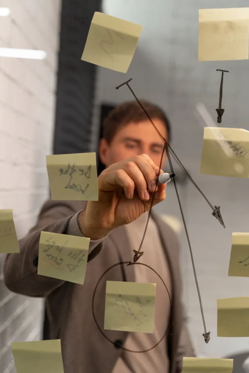 Pessoa organizando ideias e estabelecendo metas em um quadro com post-its para melhorar a produtividade.