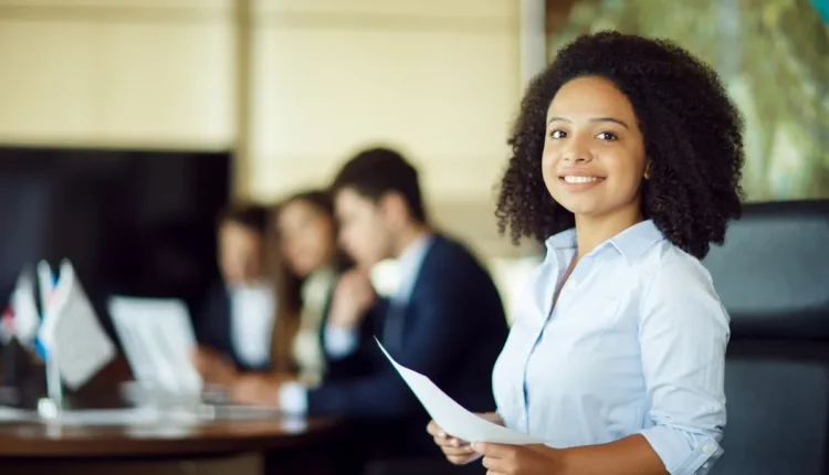 Jovem sorridente segurando documentos em um ambiente de trabalho durante uma feira de empregos.