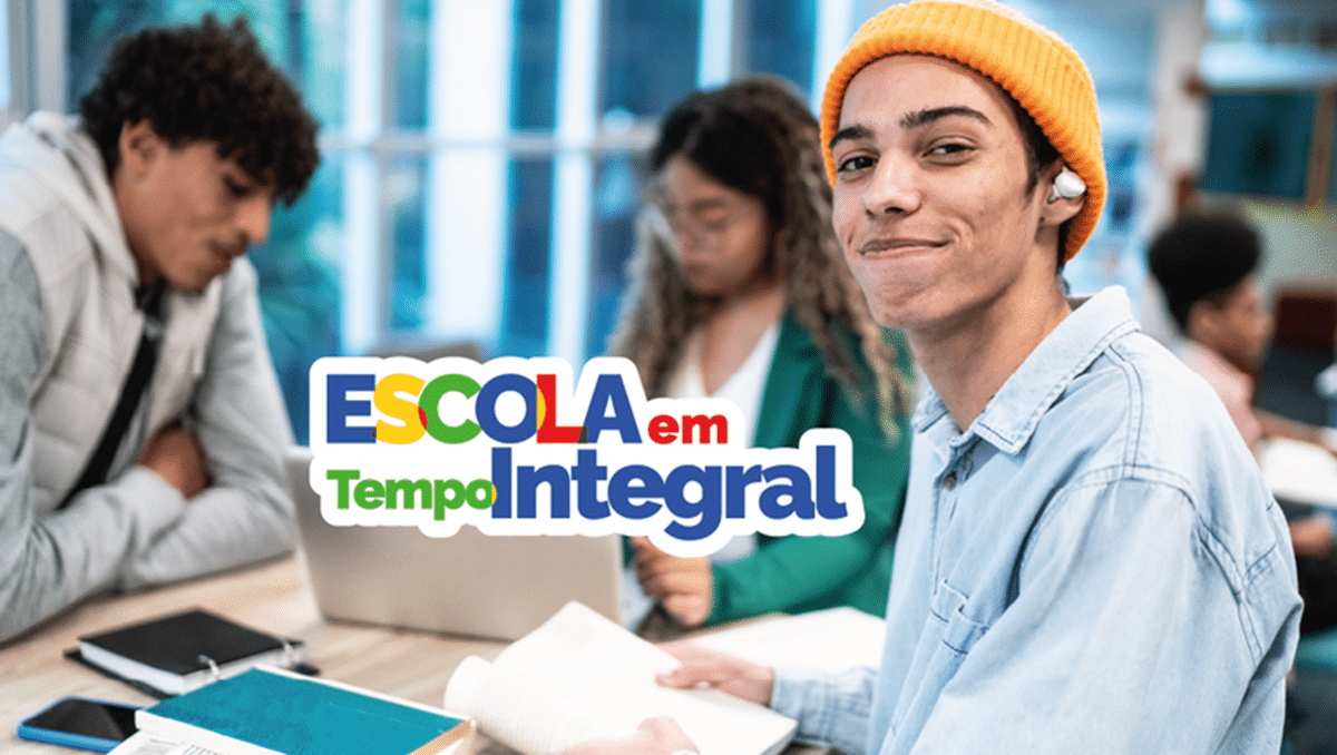 Jovem estudante com gorro amarelo sorrindo em sala de aula com outros alunos ao fundo.