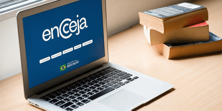 Página do Encceja aberta em notebook ao lado de livros.