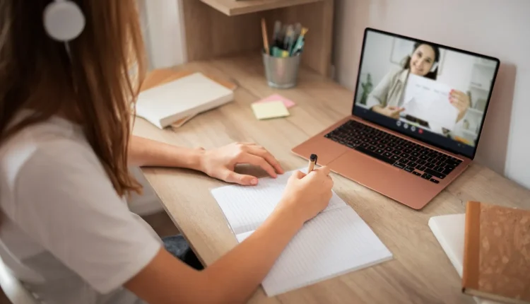 Estudante usando fones de ouvido assistindo aula online no laptop e fazendo anotações em caderno