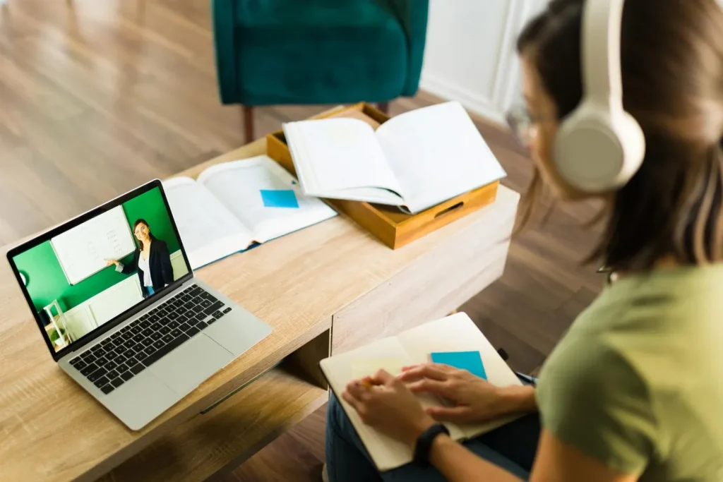 Aluna participa de aula online com professora explicando conteúdo em quadro branco