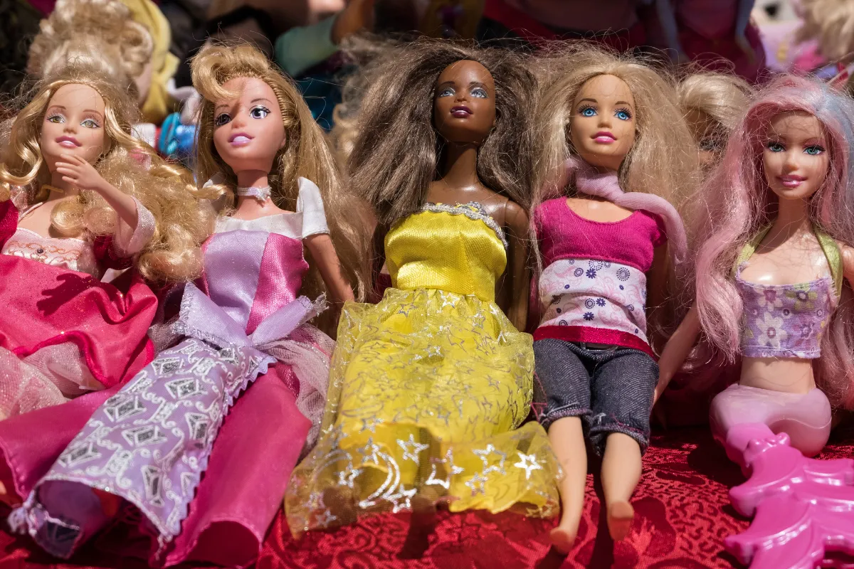 Bonecas Barbie usadas com roupas coloridas expostas em uma superfície vermelha.